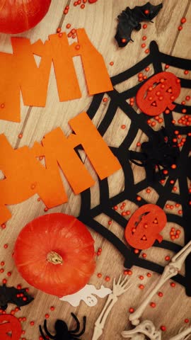 Halloween decoration with bats, pumpkins, spiders web and skeleton on wooden background. Scary Halloween pumpkins. Vertical video