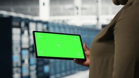 IT professional in data center using green screen tablet to ensure error free supercomputers networks. African american woman uses mockup device to monitor server hub gear parts for failures, camera B - Powered by Shutterstock - Get 15% off with code: PIKWIZARD15