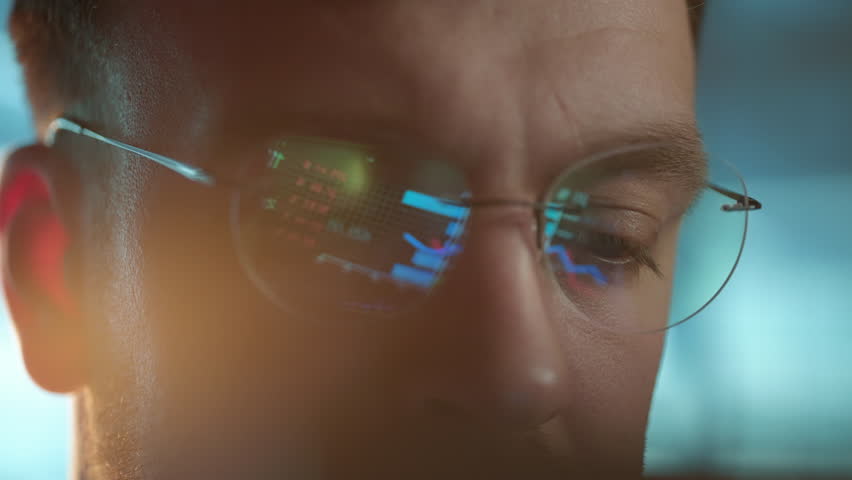 Trader wearing glasses is working on laptop computer. Screen with stock market charts and Bitcoin BTC or Ethereum ETH data analysis reflection. Broker trading online. Altcoins crypto currency trading
