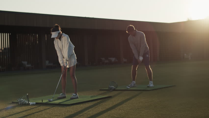 Partners swing golf clubs sending balls to goals at sports center