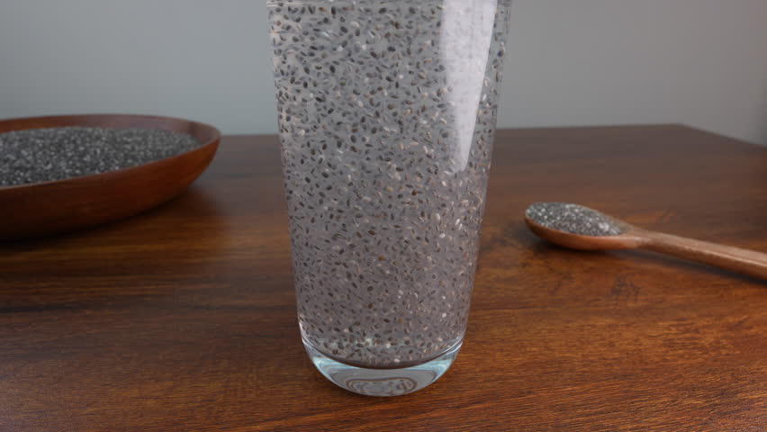 Clear glass filled with hydrated chia seeds creating gel-like texture with wooden kitchen utensils