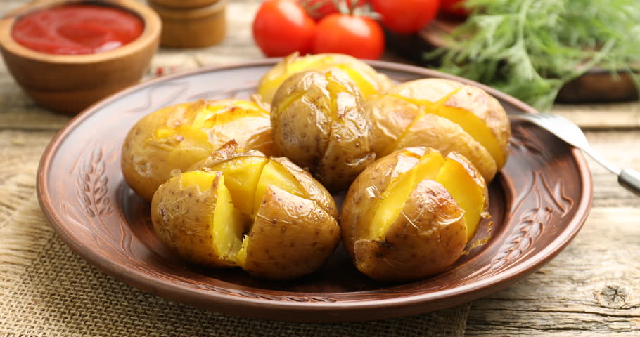 Woman peppering tasty baked potatoes at wooden table, closeup