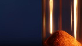 Hourglass bulb with rapidly pouring sand, close-up on a dark blue background, concept of fast time flow. - Powered by Shutterstock - Get 15% off with code: PIKWIZARD15