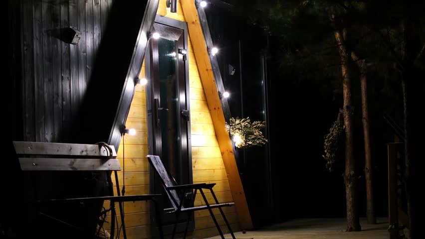 Cozy cabin exterior illuminated by warm lights at night, showcasing wooden textures and inviting ambiance, creating a serene atmosphere for relaxation and connection with nature