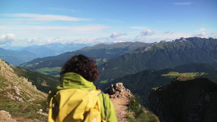 Hiker with yellow jacket looking at panoramic Dolomites mountain landscape in Italy