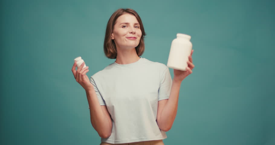 Beautiful young happy woman with choosing what vitamins to take on blue background.
