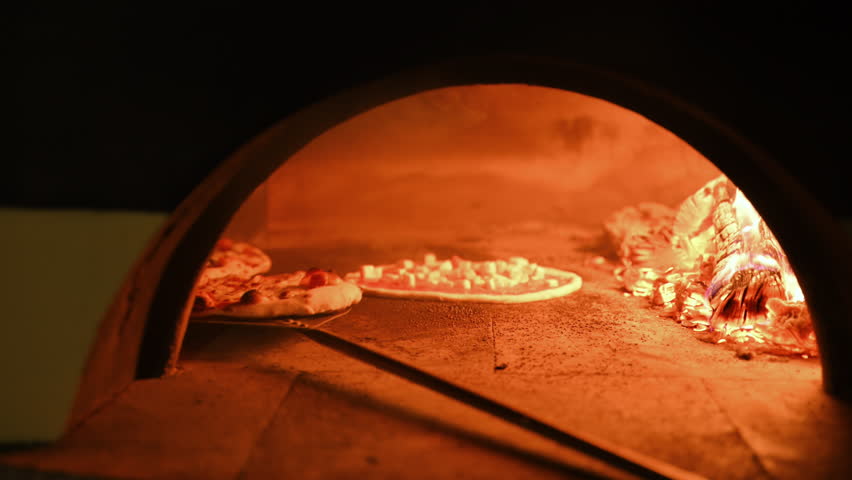 Chef is placing Italian pizza in the oven with wooden fire and smoke, wood stove oven in the restaurant