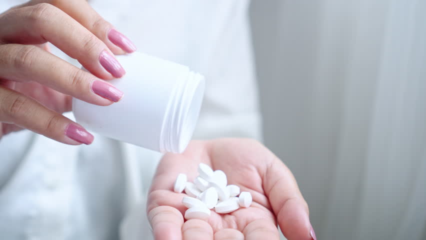 Close-up of a woman’s hand holding a bottle of medicine while taking pills. Concept highlighting overdose risk with paracetamol or painkillers, proper medication use, and health care awareness