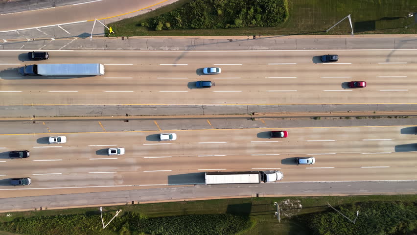Highway road with the fast-moving vehicles, trucks showing U.S. transportation infrastructure under a bright sky. Drone horizontal view.