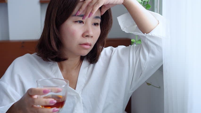 Stressed Asian woman drinkin a whiskey glass, feeling depressed concept of alcoholism, addiction, and unhealthy drinking habits, emotional struggles affecting mental 