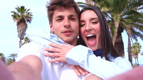 Happy young couple outdoors with palm trees, smiling and posing for selfie, lifestyle, romance, leisure, modern love, summer fun, digital connection, online sharing, social media, cheerful emotions - Powered by Shutterstock - Get 15% off with code: PIKWIZARD15