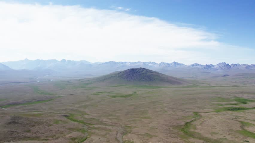 A lone hill rises from the vast Deosai plains surrounded by distant mountain ranges. Deosai, Pakistan