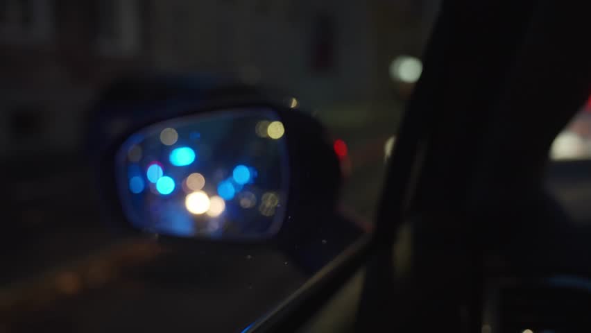 View of ambulance with flashing blue lights reflected in car side mirror at night. Concept of emergency, rescue and traffic safety