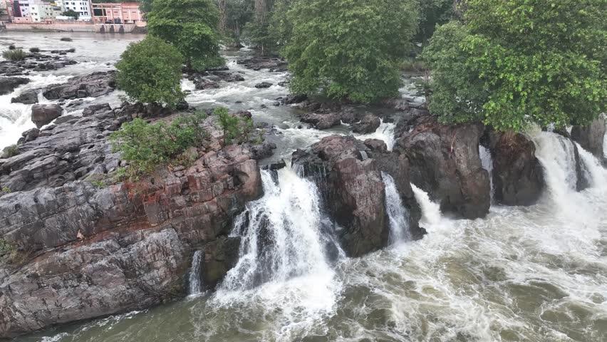 Aerial footage of multiple waterfalls flowing over rocks into a scenic river valley, surrounded by greenery. Stunning drone view of Indian natural wonder.