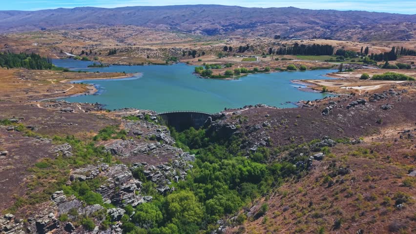 Drone reversing upward from Manorburn Dam showing reservoir, valley, and surrounding mountains.