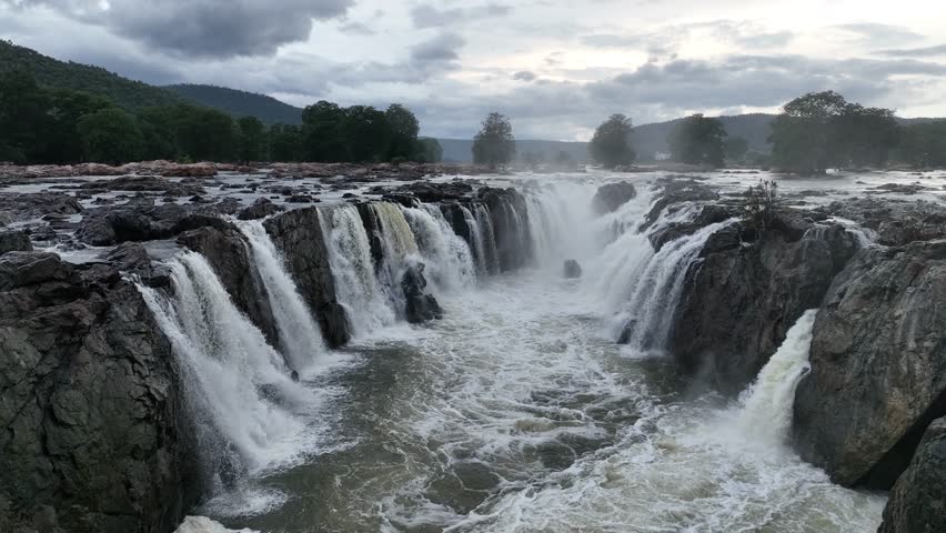 Aerial footage of multiple waterfall streams cascading over rocky cliffs in South India. Scenic natural wonder, monsoon water flow, and a popular travel attraction.