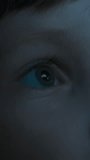 Close-up of a little boys eye, lit by the blue light of the cinema screen, with a reflection in his eye, as he watches intently and curiously at the movie on the TV, tablet, or plays computer games  - Powered by Shutterstock - Get 15% off with code: PIKWIZARD15
