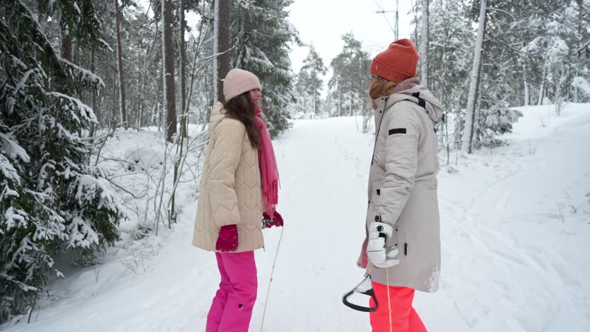Middle-aged mother and teenage daughter enjoying walk in snowy Finland forest. Warm clothing, family values, lifestyle, togetherness and joyful winter holiday season atmosphere.