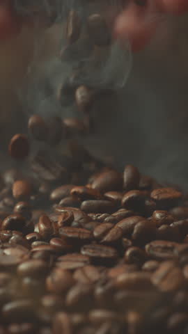 Super slow motion shot of falling roasted coffee beans from hand with smoke in macro. Vertical close up video