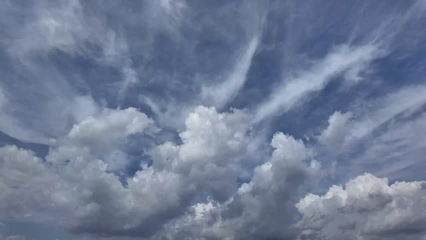 A Timelapse of a fast changing sky cloudscape, with white cottony clouds evolving in a blue sky, with clouds coming from various directions.