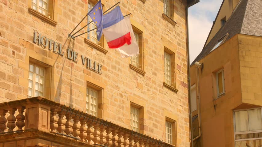 Capture the essence of Brive with views of the town hall featuring proudly displayed French flags. The warm sunlight highlights the stone architecture, reflecting a classic European vibe.