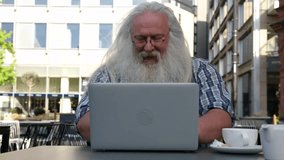 Elderly man enjoys coffee while working on laptop outdoors in a lively city plaza during a sunny day - Powered by Shutterstock - Get 15% off with code: PIKWIZARD15