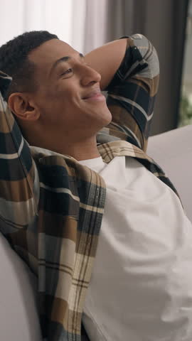 Smiling resting calm African American man guy ethnic male enjoy air conditioner indoors relaxing at home sofa couch leaning back holding hands behind head homeowner napping closed eyes loan mortgage