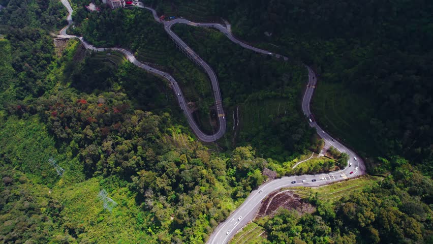 Wide drone shot capturing curving roadway built along a mountainous landscape.