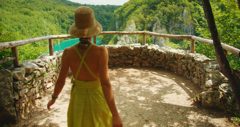 Woman in a summer dress overlooks a turquoise lake in a lush canyon Plitvice Lakes National Park Croatia