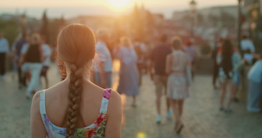 Woman walking among crowd on Charles Bridge in Prague at sunset during summer evening