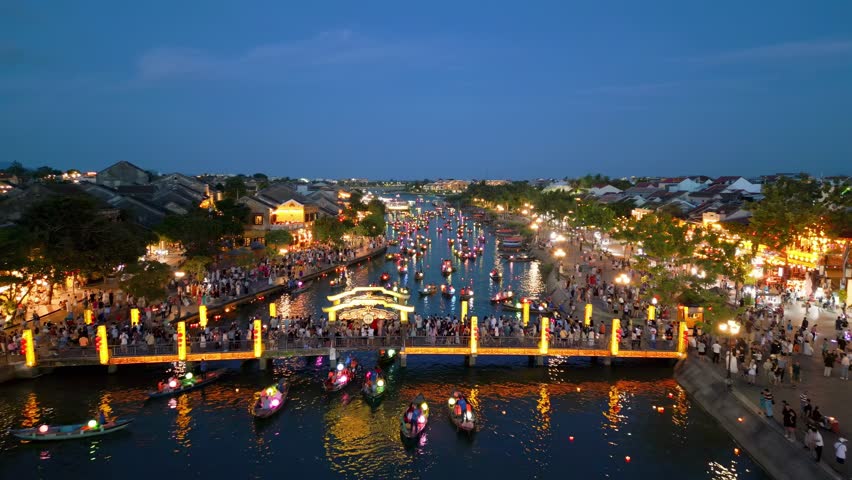 Aerial drone view of Hoi An ancient town in Vietnam, between the traditional old houses, and along the river filled with colorful boats with lanterns and tourist visitors.