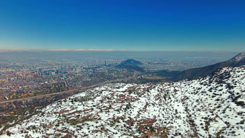 Aerial reveals Santiago de Chile city below Snowed Andean Cordillera Mountain, Manquehue Hill