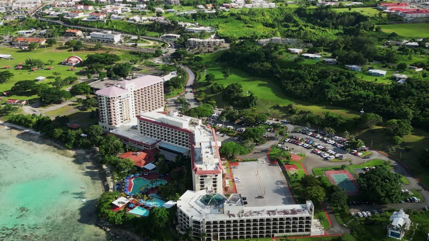 Orbiting aerial view of scenic, coastal hotel resort building and parking lot during daytime at Guam island, USA.