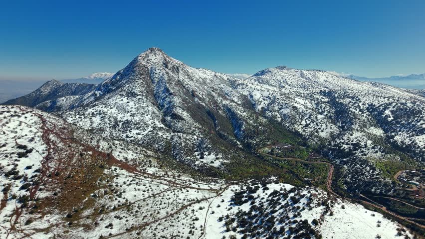 Expansive aerial view captures snowy Manquehue hill rising over Santiago landscape in Chile.