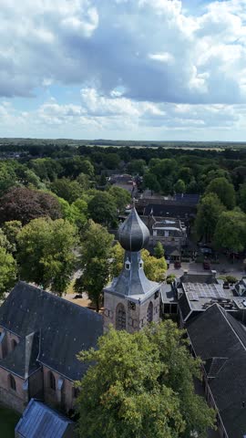 Aerial view with drone of the Church of Dwingeloo in Drenthe, Netherlands, featuring its iconic onion-shaped tower surrounded by lush trees and a charming village