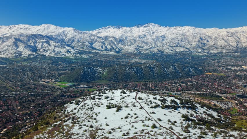Drone discovers Andean Santiago de Chile City below Snowed Cordillera Mountain Chain, Los Trapenses neighborhood