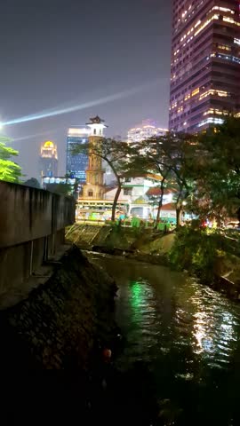Urban river at night and dark concept. The river flows with reflections from lights and is illuminated by street lights, transportation and buildings. Urban activities and the river environment