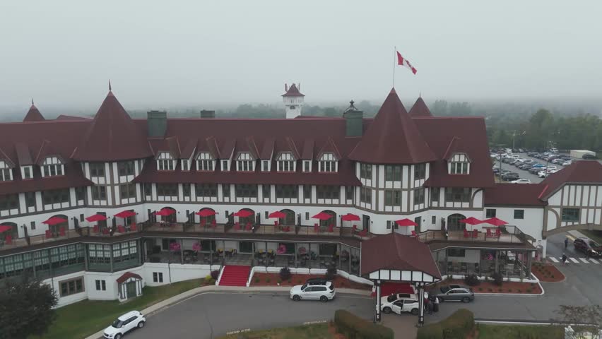 A 4K aerial view of an 1800s historic hotel with steep red roofs and white walls, glowing softly in the early morning light under a misty sky