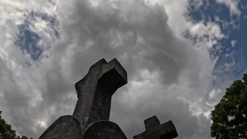 Multi-layered rainclouds swirl over a broken gravestone next to a second stone cross and tree.