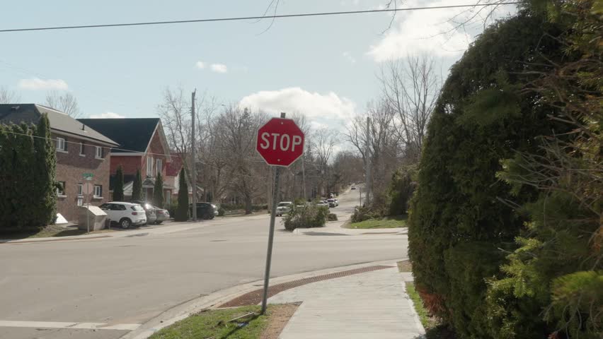 A wide zoom shot with a first person feel of walking on a sidewalk approaching a stop sign in a mature neighborhood in Orillia, Ontario, Canada