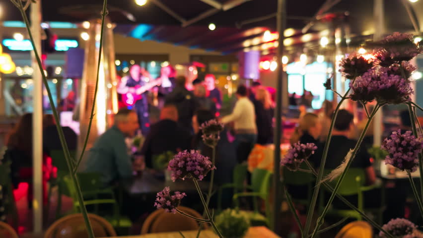 A Vibrant and Lively Evening Scene at a Cozy Restaurant Featuring Live Music and Beautiful Floral Decor