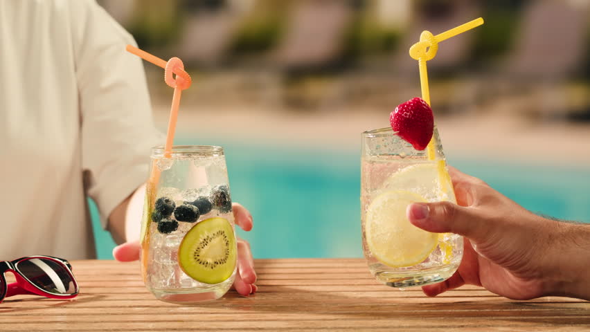 Fruit cocktail in hotel bar, Two cocktail glasses cheers in the hands on sea background. Bartenter making drink in bar, Summer vacation concept, A beautiful couple enjoy the vacation at the beach.
