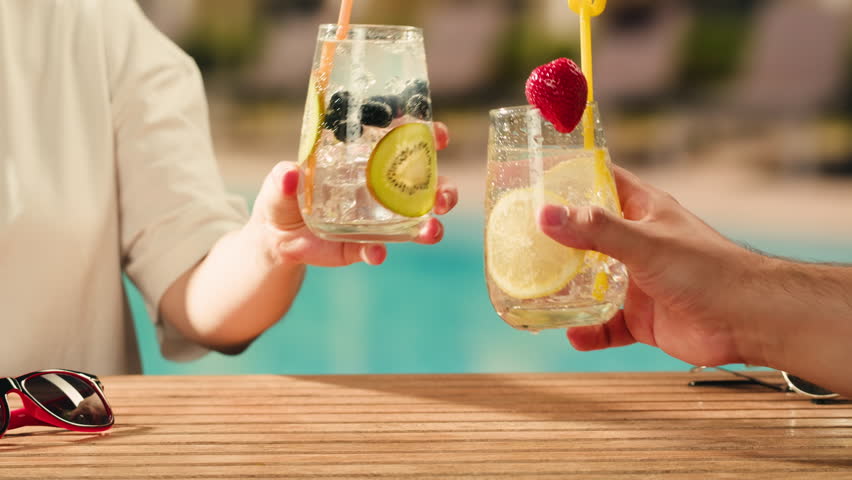 Fruit cocktail in hotel bar, Two cocktail glasses cheers in the hands on sea background. Bartenter making drink in bar, Summer vacation concept, A beautiful couple enjoy the vacation at the beach.