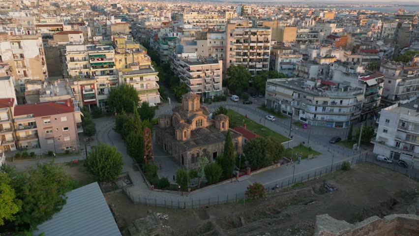Aerial views of Thessaloniki, Greece, showcase a vibrant cityscape. The camera pans over Church of Holy Apostles and modern buildings, highlighting the blend of culture and architecture