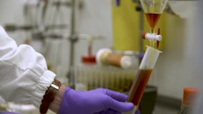 Close-up detailed view of a scientist in laboratory gloves carefully releasing orange liquid from a burette filter tap into a volumetric flask — themes of science, chemistry, precision, and analysis - Powered by Shutterstock - Get 15% off with code: PIKWIZARD15