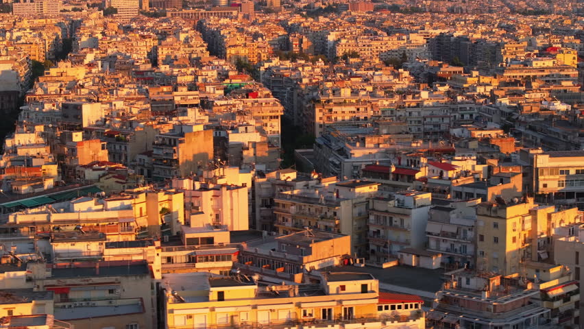 The warm hues of sunset bathe the buildings and streets of Thessaloniki, Greece. Mount Olympus is visible in the distance