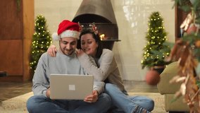 Merry Christmas Happy young adult couple with laptop near Christmas tree and fireplace. Happy family man woman searching buying gifts for Christmas or watching movie together. Preparation for holidays - Powered by Shutterstock - Get 15% off with code: PIKWIZARD15