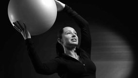 Commercial black and white video. Slow motion close-up of a fit female trainer turning her head, smiling at the camera, and performing side bends with a large fitness ball.  - Powered by Shutterstock - Get 15% off with code: PIKWIZARD15