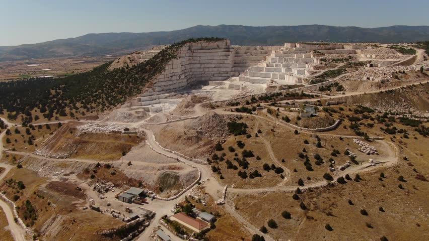 A large marble quarry in mountainous terrain. A stepped excavation structure, white stone surfaces, and an industrial contrast with the natural landscape. Karamanlı, Burdur, Turkey.