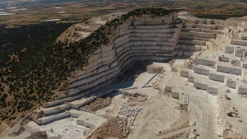 Stepped open-air marble quarry in rural terrain. Layered white rock surfaces, piles of stone, and traces of industrial landscape with surrounding texture. Karamanlı, Burdur, Turkey.